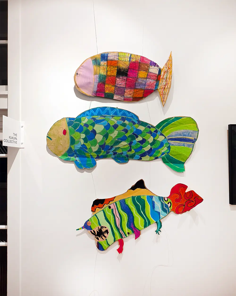 Three large cut-out fish painted by students, each one patterned differently, hung together on a gallery wall