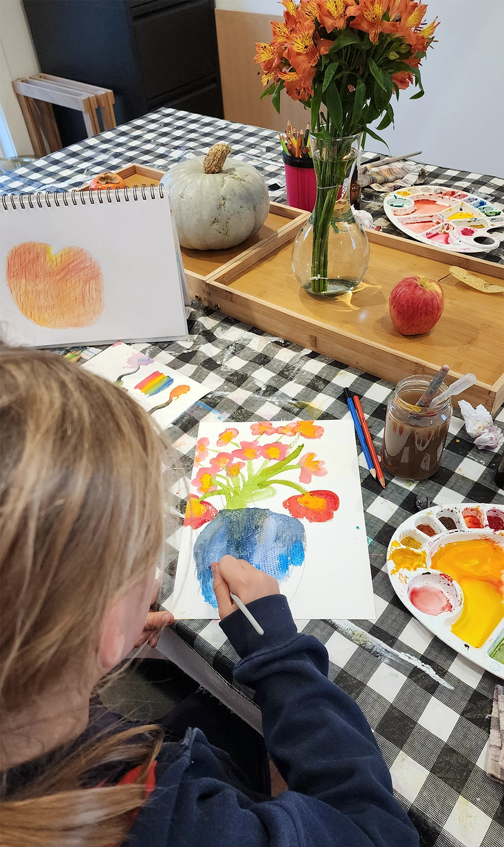 A student painting a still life of flowers and a pumpkin set up on the table
