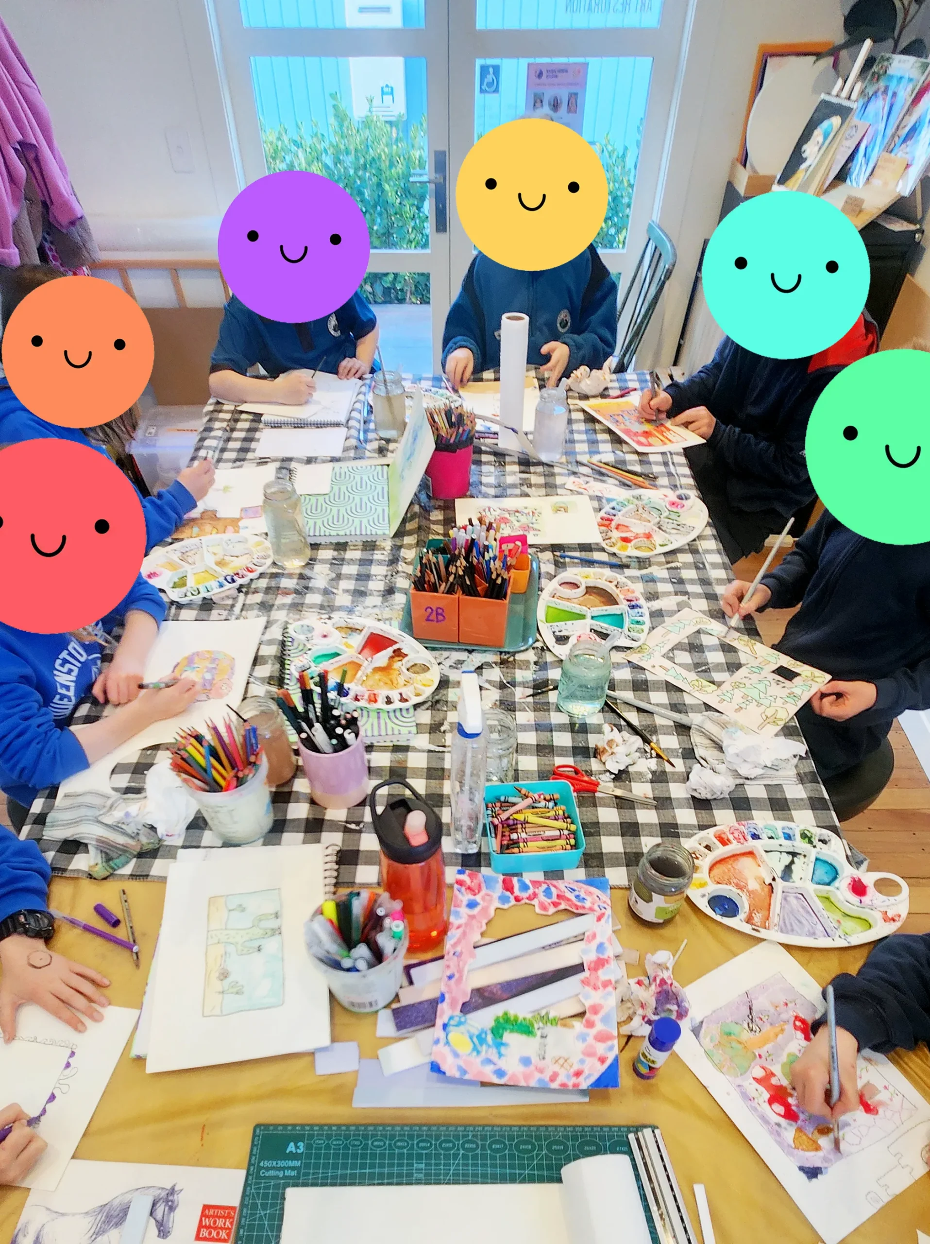 The after school art class at work around the studio table, paints and palettes spread out