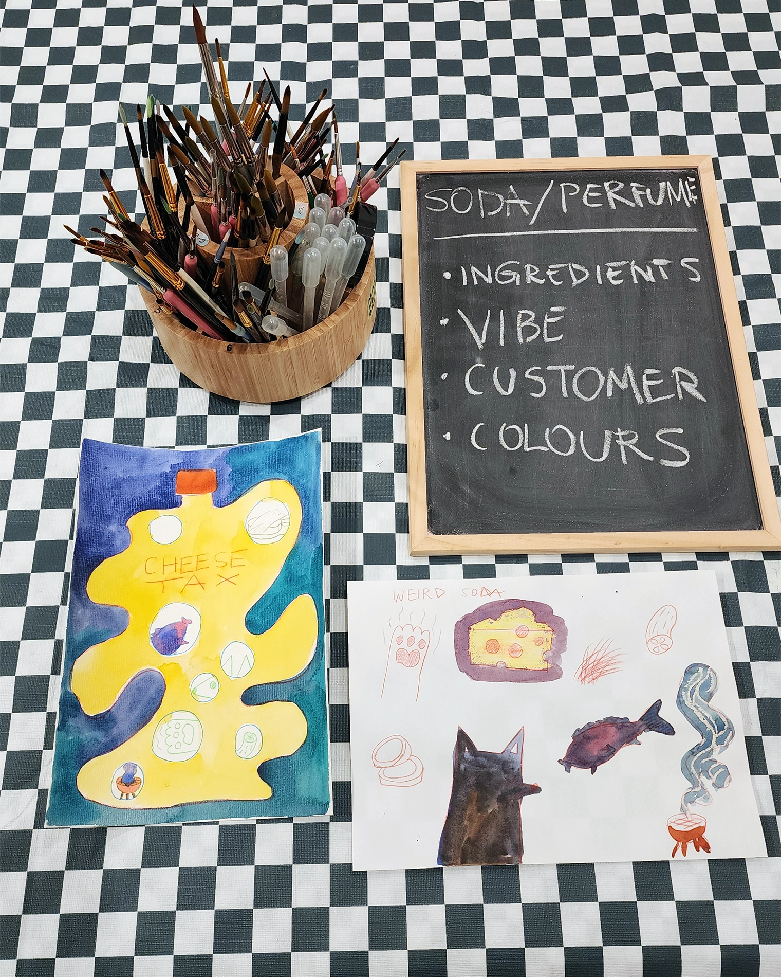 A blackboard listing the design brief - ingredients, vibe, customer, colours - beside students' soda and perfume designs