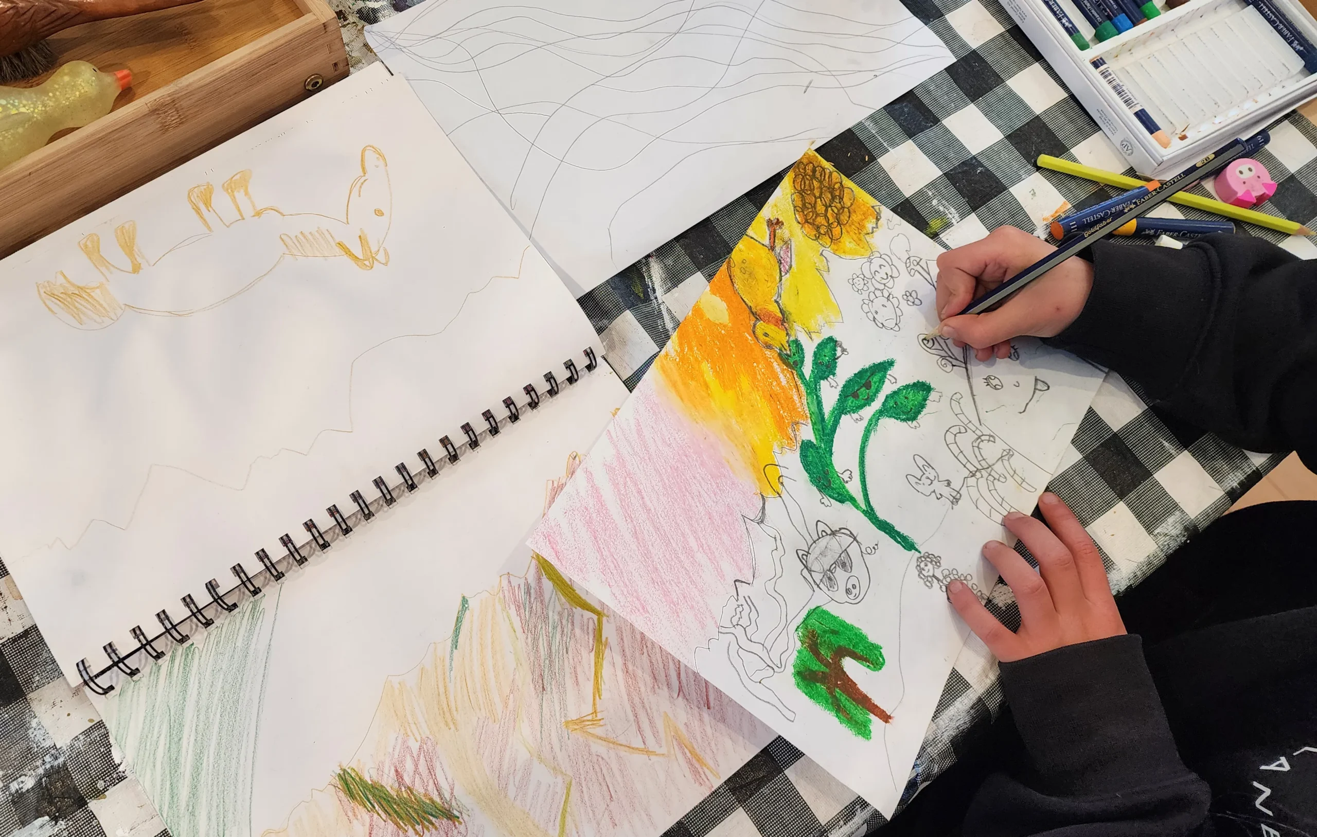 A student's sketchbook open beside a still life, with drawings worked up from it in pencil and colour