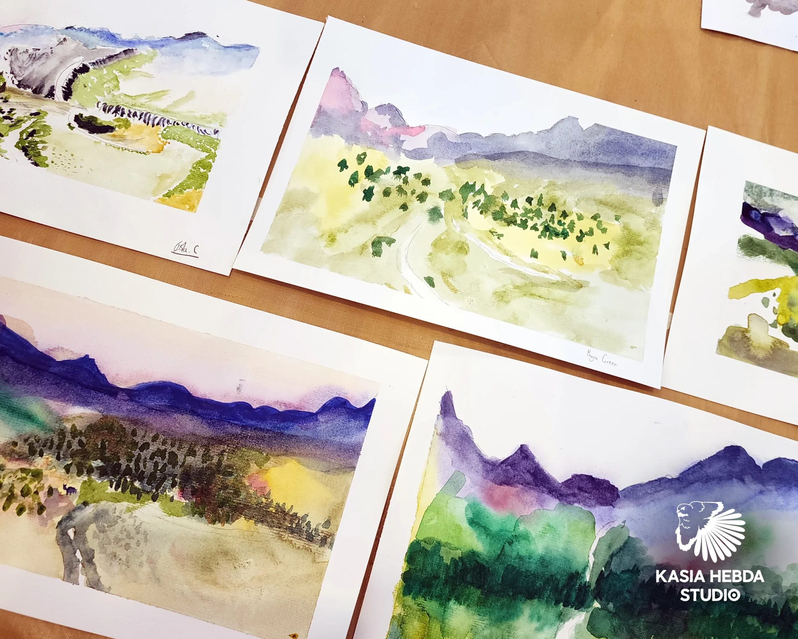 Several students' watercolour landscapes laid out side by side, each one different