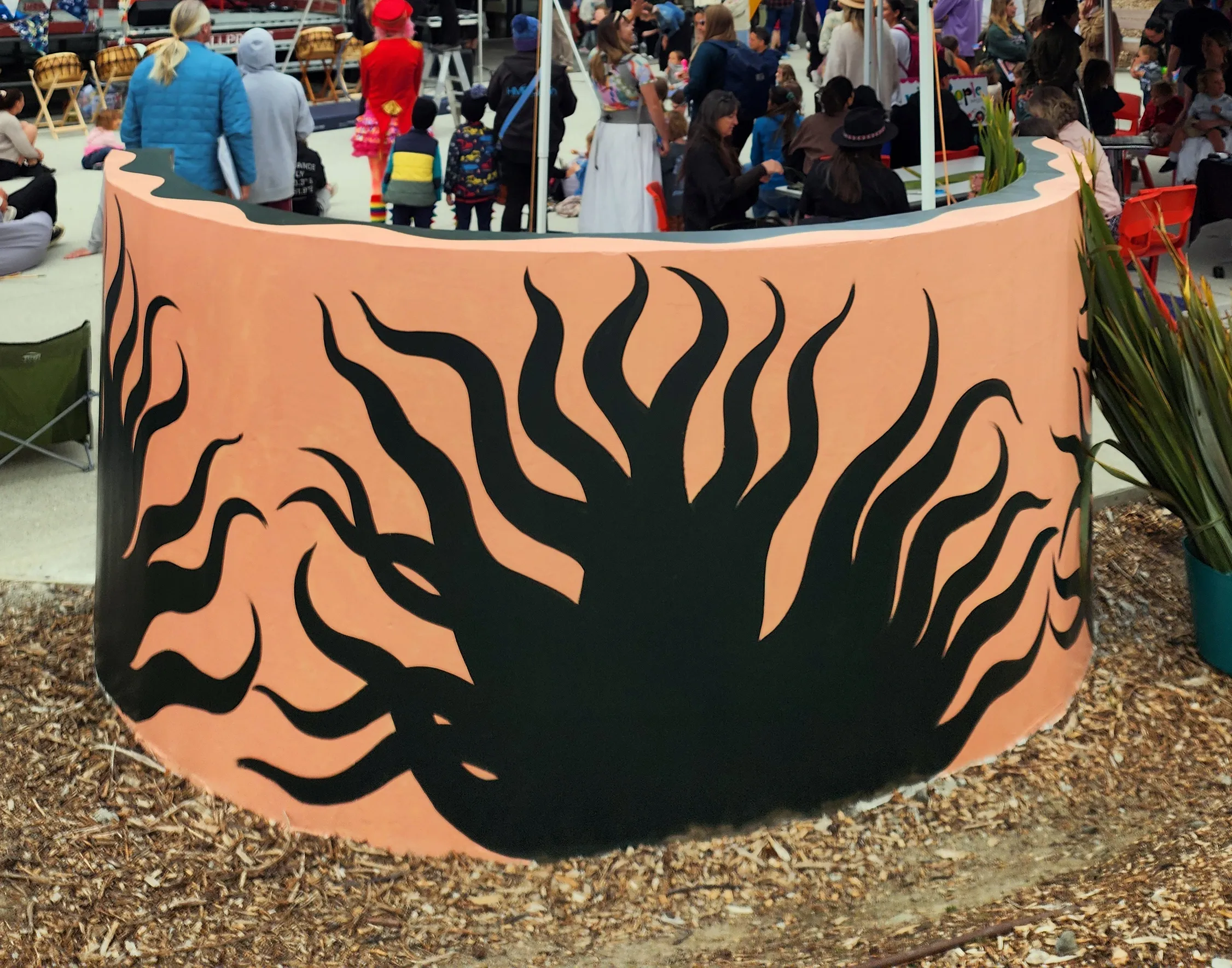 The back of the Onwards in Art! wall - a black harakeke silhouette on peach, with families gathered behind